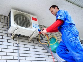 A person on a ladder fixing a air conditionerDescription automatically generated