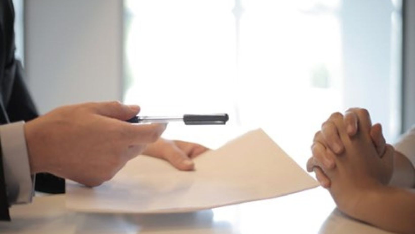 Two people sitting across each other; one holding a paper and a pen