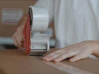 A person sealing a cardboard box with a tape