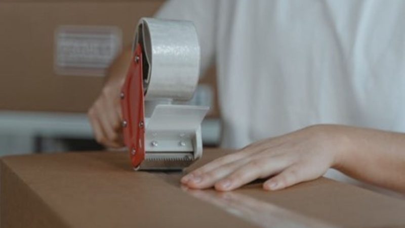 A person sealing a cardboard box with a tape