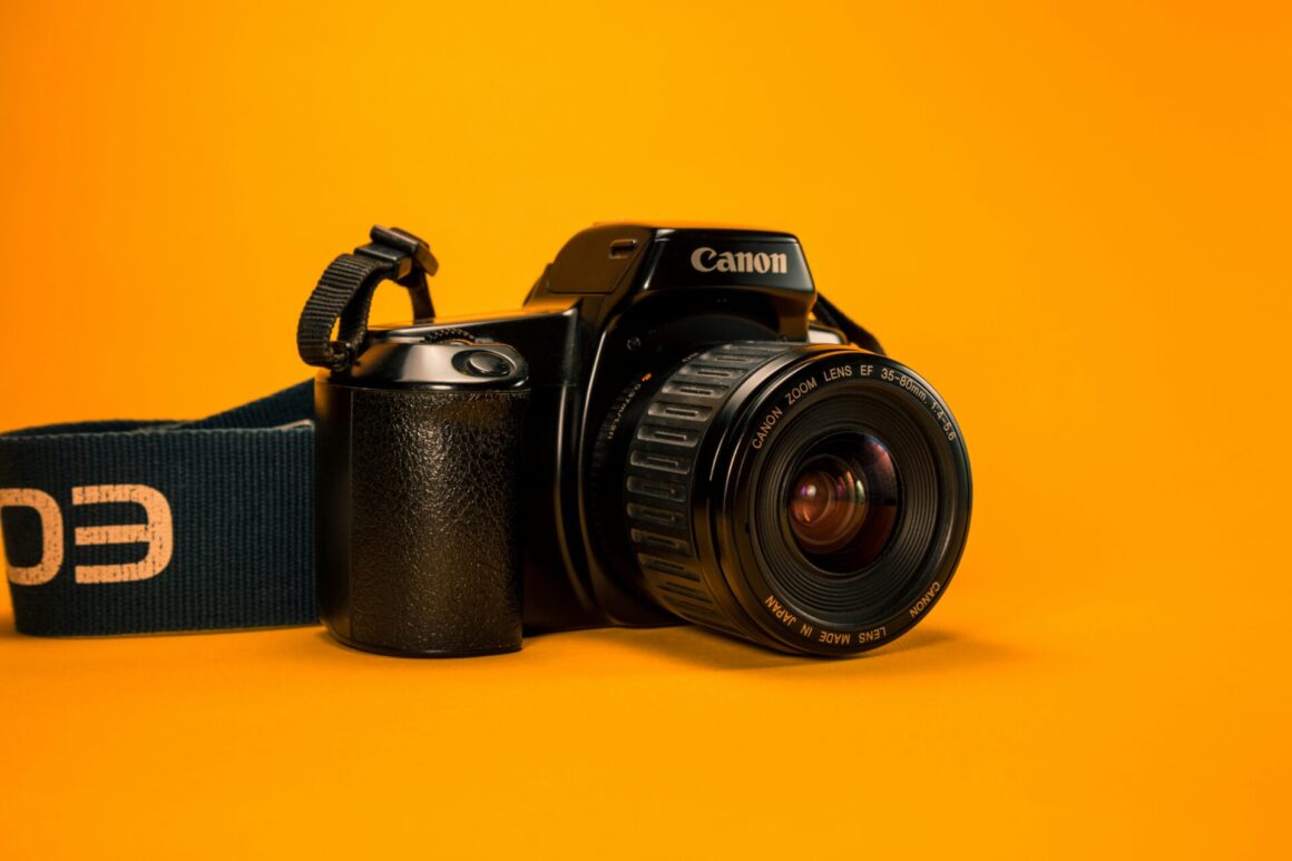 A black Canon DSLR camera with a zoom lens, on an orange surface and background.