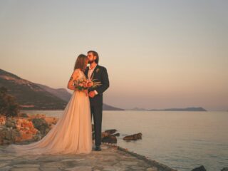 A wedding photo of a couple near the shoreline, at dusk.
